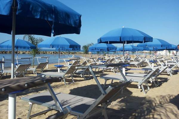 Reihe von Sonnenliegen mit blauen Umbrellas am Strand in Acacia Marina Hotel