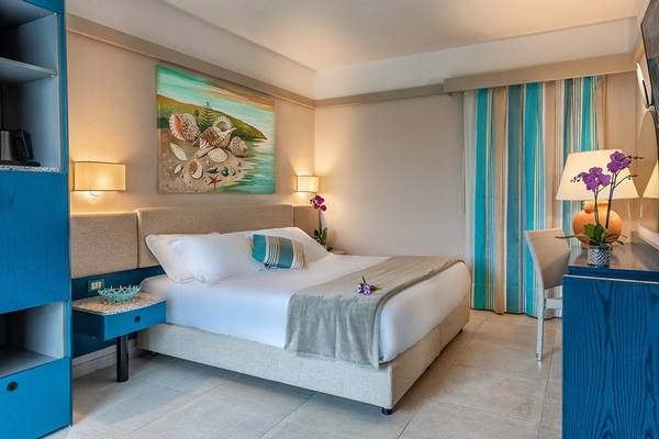 Innenansicht eines Hotelzimmers im Acacia Marina Hotel mit Doppelbett, blauen Möbeln und Meereslandschaftsbild.