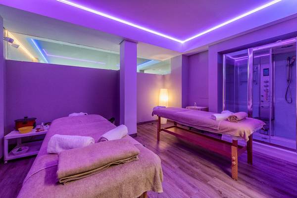 Spa-Behandlungsraum mit Massagebetten und Dusche, lila Beleuchtung.