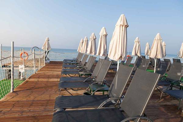 Reihe von Liegestühlen auf einer Holzplattform am Meer mit geöffneten Sonnenschirmen.