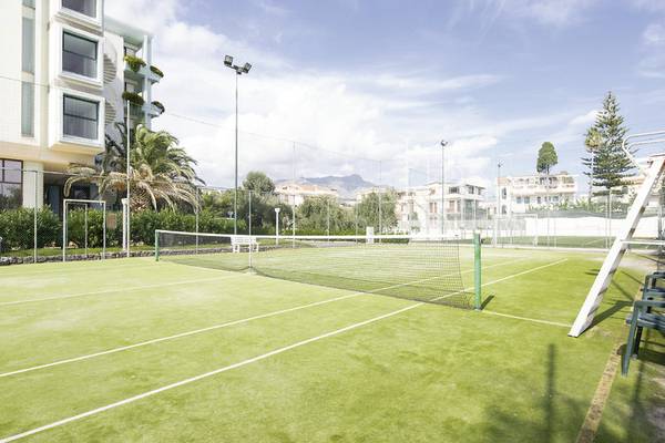 Tennisplatz vor dem UNAHOTELS Naxos Beach Sicilia Hotel mit Netz, Bänken und Gebäude im Hintergrund.