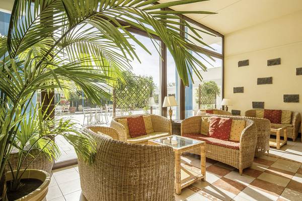 Loungebereich des UNAHOTELS Naxos Beach Sicilia mit Korbstühlen, einem Glastisch und großen Palmen.