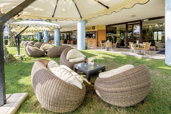 Gartenlounge mit Korbsesseln und Tischen im Freien beim UNAHOTELS Naxos Beach Sicilia.