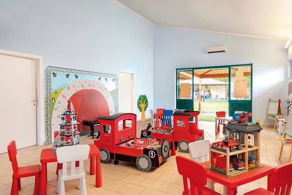 Kinderspielzimmer im UNAHOTELS Naxos Beach Sicilia mit roten Spielzeugzügen und Möbeln.