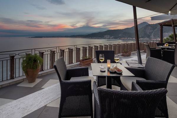 Ausblick von der Terrasse des UNAHOTELS Capotaormina mit Meer, Bergen und Sonnenuntergang.