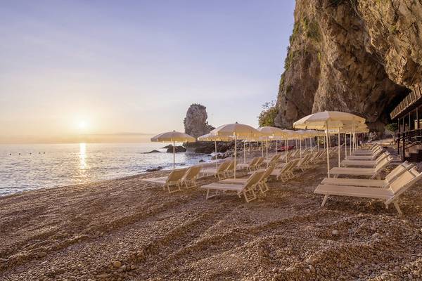 Sonnenuntergang am Strand des UNAHOTELS Capotaormina mit Sonnenschirmen und Liegen.