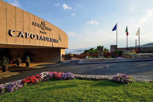 Außenansicht des UNAHOTELS Capotaormina mit gepflegtem Rasen und Blumenbeet.
