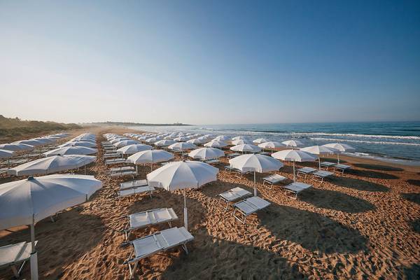 Strand des VOI Marsa Siclà Essentia Hotels mit vielen weißen Sonnenschirmen und Liegen.