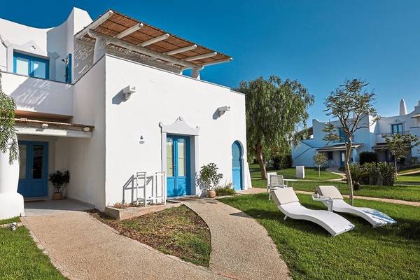 Außenansicht des VOI Marsa Siclà Essentia Hotels, eine weiße Villa mit blauen Türen und Fenstern vor einem grünen Rasen.