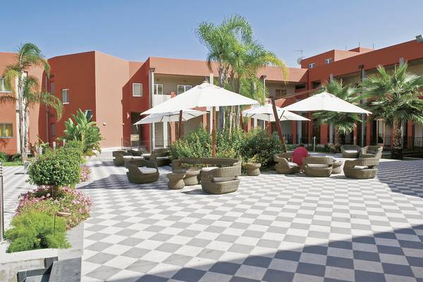 Außenbereich des VOI Baia di Tindari Resorts mit geometrischem Boden, Lounge-Sesseln und Sonnenschirmen.