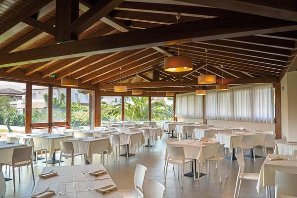 Innenbereich des Restaurants im VOI Baia di Tindari Resort mit vielen weißen Tischen und Stühlen.