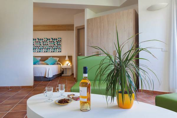 Innenansicht eines Hotelzimmers im VOI Arenella Resort mit Bett, Pflanzen und Tisch.