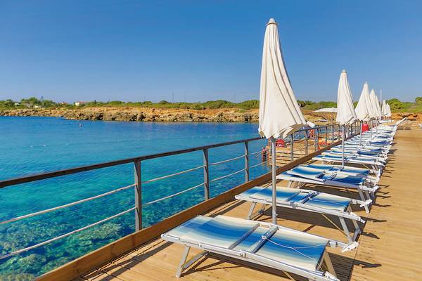 Reihe von Sonnenliegen auf einer Terrasse am Wasser im VOI Arenella Resort