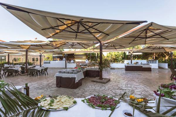 Außenbereich des VOI Arenella Resorts mit großen Sonnenschirmen und einem Tisch voller Speisen.
