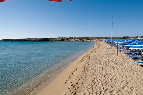 Strand des VOI Arenella Resorts mit vielen Sonnenschirmen und Liegen am Meer.