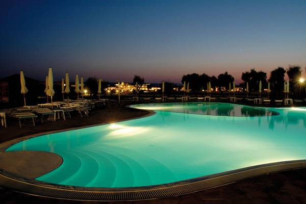 Beleuchteter Pool im VOI Arenella Resort bei Nacht mit Sonnenliegen und Schirmen.
