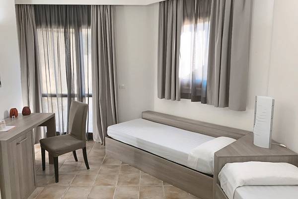 Innenansicht eines Doppelzimmers im VOI Arenella Resort mit zwei Einzelbetten, Schreibtisch und Stuhl.