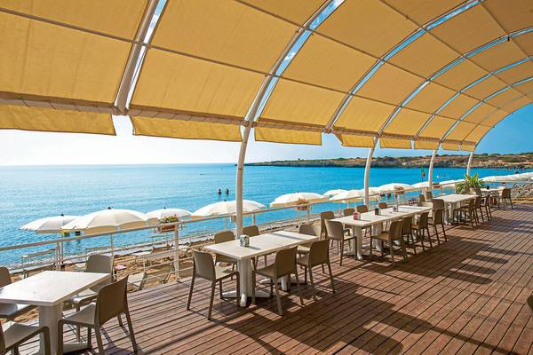 Außenterrasse des VOI Arenella Resorts mit Blick auf das Meer und weißen Sonnenschirmen.