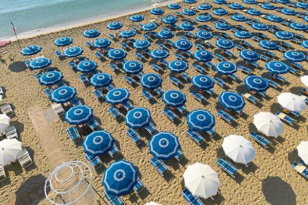 Luftaufnahme des VOI Arenella Resorts Strand mit vielen blauen und weißen Sonnenschirmen.
