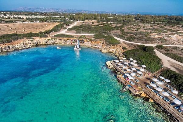 Luftaufnahme des VOI Arenella Resorts mit Blick auf eine blaue Lagune und eine Holzpromenade mit Sonnenschirmen.