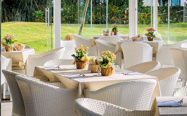 Restaurantterrasse im Acacia Palace Hotel mit weißen Tischen und Stühlen und Blick auf den Rasen