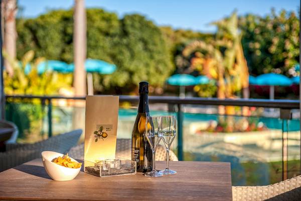 Terrasse im Acacia Palace Hotel mit einer Flasche und zwei Weinglaesern und einem Schwimmbad im Hintergrund