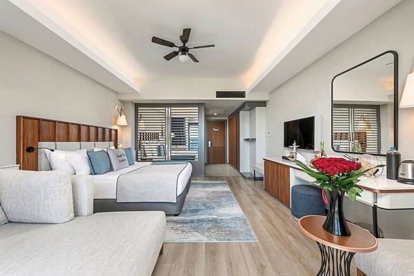 Innenansicht eines Hotelzimmers im Seaden Quality Resort & Spa mit Bett, Sofa, Teppich, Schreibtisch und Fernseher.