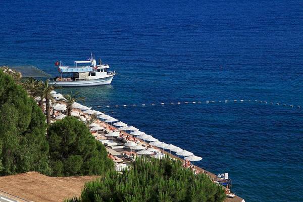 Aussicht auf den Strand des Larissa Bodrum View Resorts mit vielen Sonnenschirmen und einer weißen Boot vor dem Meer.