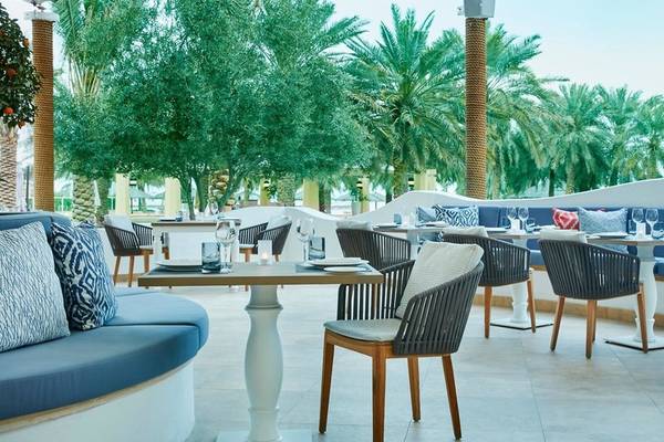 Außenbereich des Intercontinental Doha Beach & Spa mit Tischen, Stühlen und Palmen.