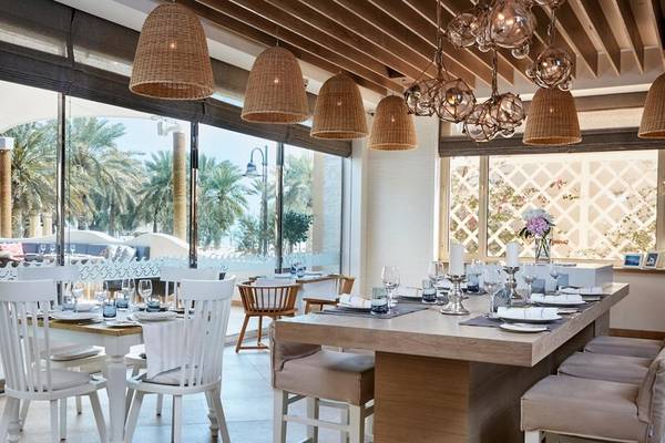Ein elegantes Esszimmer im Intercontinental Doha Beach & Spa Hotel mit weißen Stühlen und Tischen, rustikalen Holzlampen und großen Glasfenstern.