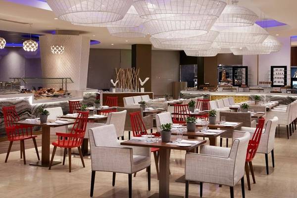 Innenansicht des Restaurants im Intercontinental Doha Beach & Spa Hotel mit geometrischen Leuchten, gedeckten Tischen und roten Stühlen.