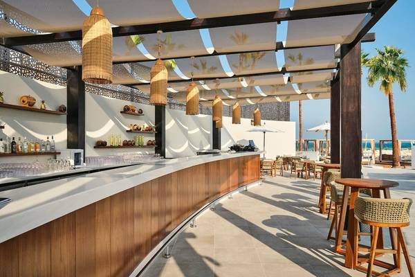 Hotelterrasse des Intercontinental Doha Beach & Spa mit Bar, Tischen und Stühlen unter Sonnenschirmen.