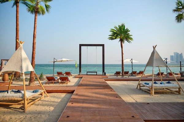 Strandbereich des Intercontinental Doha Beach & Spa mit Liegestühlen, Palmen und einem Blick auf das Meer.