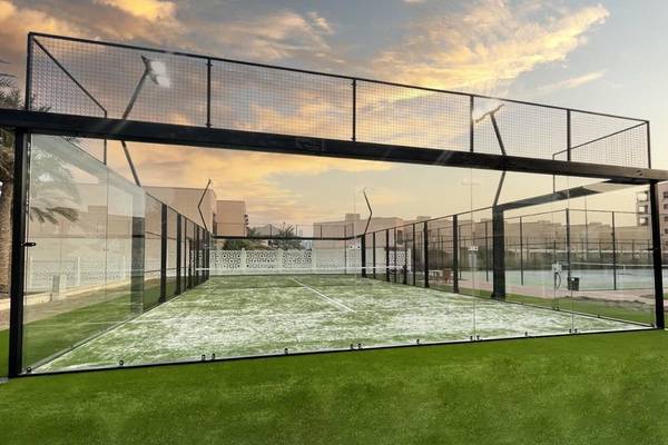 Tennisplatz im Intercontinental Doha Beach & Spa Hotel, eingezäunt mit Glaswänden und grünem Kunstrasen.