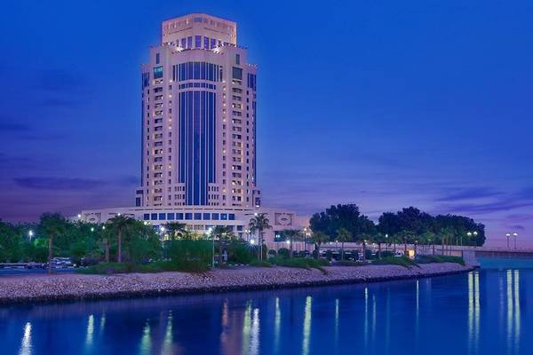 Das Ritz-Carlton Doha Hotel bei Nacht mit vielen Lichtern und Wasser im Vordergrund.