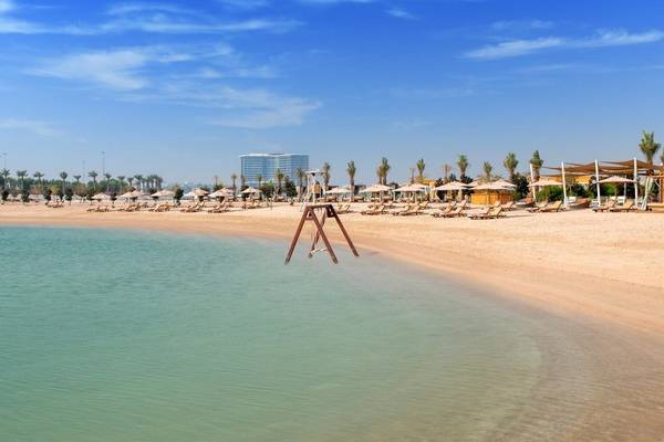 Strand des Ritz-Carlton Doha mit vielen Liegestühlen und Palmen am Wasser