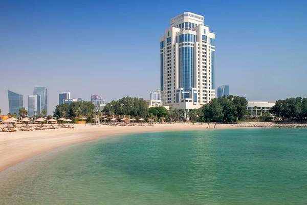 Strand mit kristallklarem Wasser und The Ritz-Carlton Doha Hotel im Hintergrund.