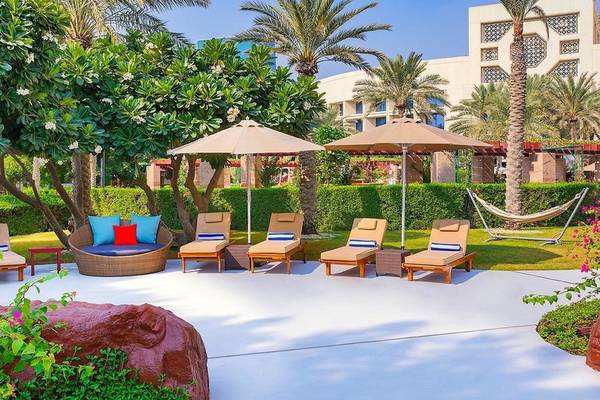 Außenbereich des Ritz-Carlton Doha mit Lounge-Sesseln, Sonnenschirmen und Palmen im Hintergrund.