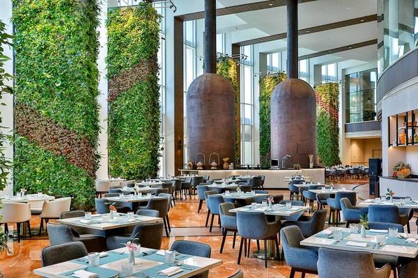 Innenbereich des Restaurants im Ritz-Carlton Doha mit grünen Wänden und runden Holzsäulen.