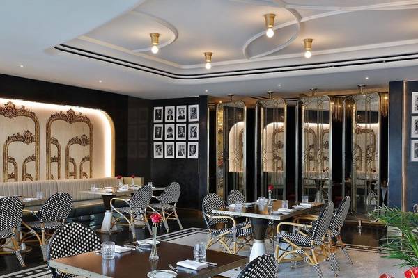 Innenbereich des Restaurants im Ritz-Carlton Doha mit schwarzen und weißen Stühlen und Tischen, goldenen Verzierungen und Fotowänden.