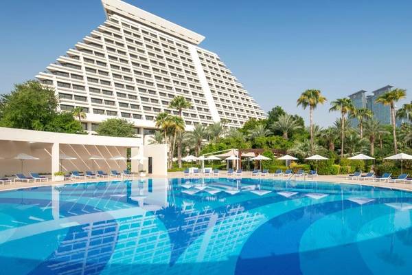Ein Swimmingpool vor dem Sheraton Doha Resort Convention Hotel mit Sonnenliegen und Sonnenschirmen.