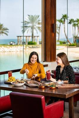 Zwei Frauen essen in einem Restaurant des Sheraton Doha Resort Convention Hotel mit Blick auf das Meer.