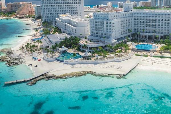 Luftaufnahme des Riu Palace Las Americas Hotels am Strand mit Swimmingpools und weißen Liegestühlen.