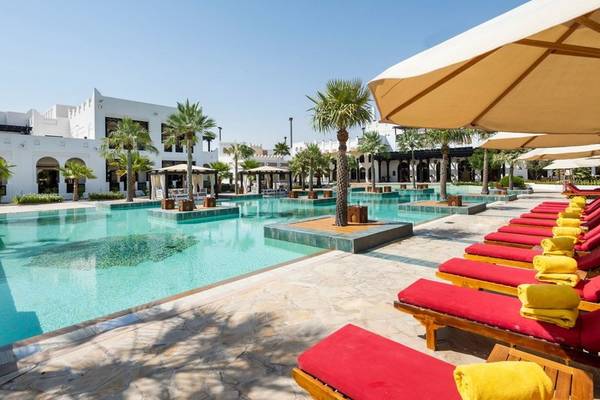 Außenpool des Sharq Village and Spa Hotels mit roten Liegestühlen und Sonnenschirmen.