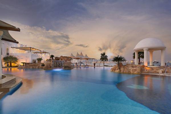 Außenpool des Sharq Village und Spa Hotels mit umliegenden Gebäuden und einer Aussicht auf die Stadt.