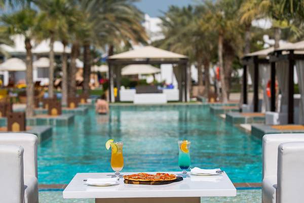 Ein Swimmingpool im Sharq Village und Spa mit einem Tisch, auf dem eine Pizza und zwei Cocktails stehen.