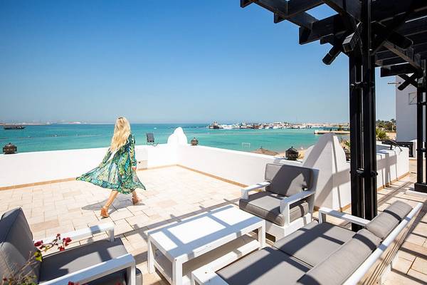Frau auf dem Balkon eines Hotels mit Blick auf das Meer und Segelboote in der Ferne.