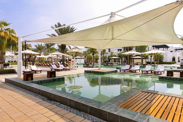 Außenpoolbereich des Sharq Village und Spa, A Ritz Carlton Hotel mit Sonnenliegen und Schirmen