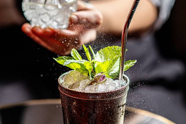 Cocktail mit Minze und Eis in einem Glas, das von einer Person geschüttelt wird.