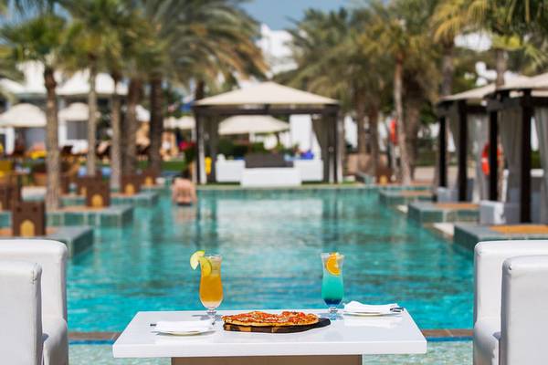 Ein Tisch neben dem Pool im Sharq Village Hotel mit einer Pizza und Getränken.